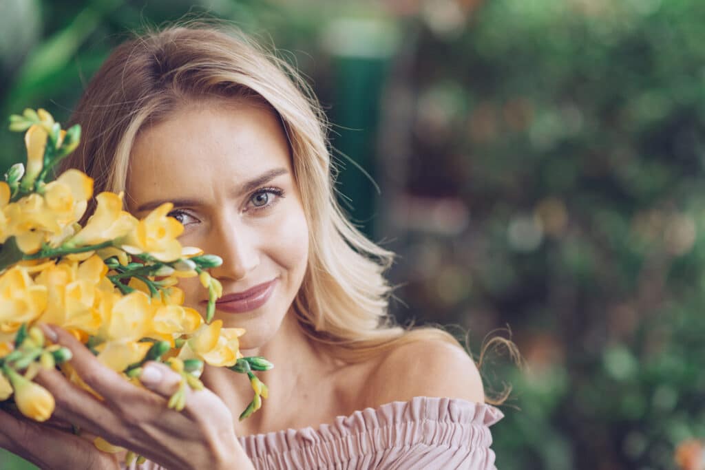 Glimlachende vrouw met gele freesia's voor haar gezicht